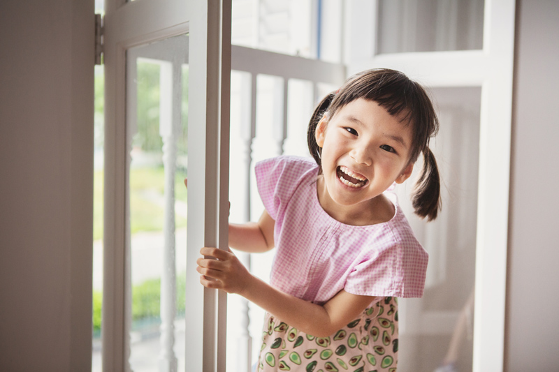 Happy little girl playing peek-a-boo with shophouse window