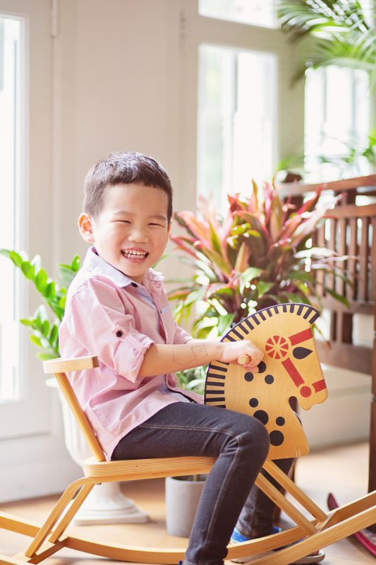 Happy little boy on rocking horse in Oh Dear Studio with lush greenery and natural light