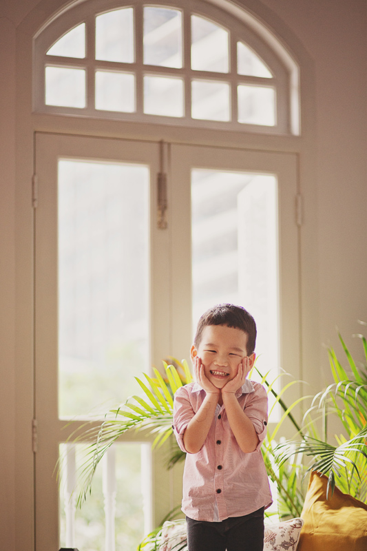 Happy little boy in Oh Dear Studio with tall glass window and lush greenery behind