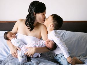 new mother with twins newborn kissing three years old toddler son