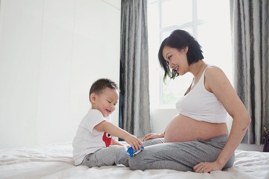 toddler and pregnant maternity mama playing on bed