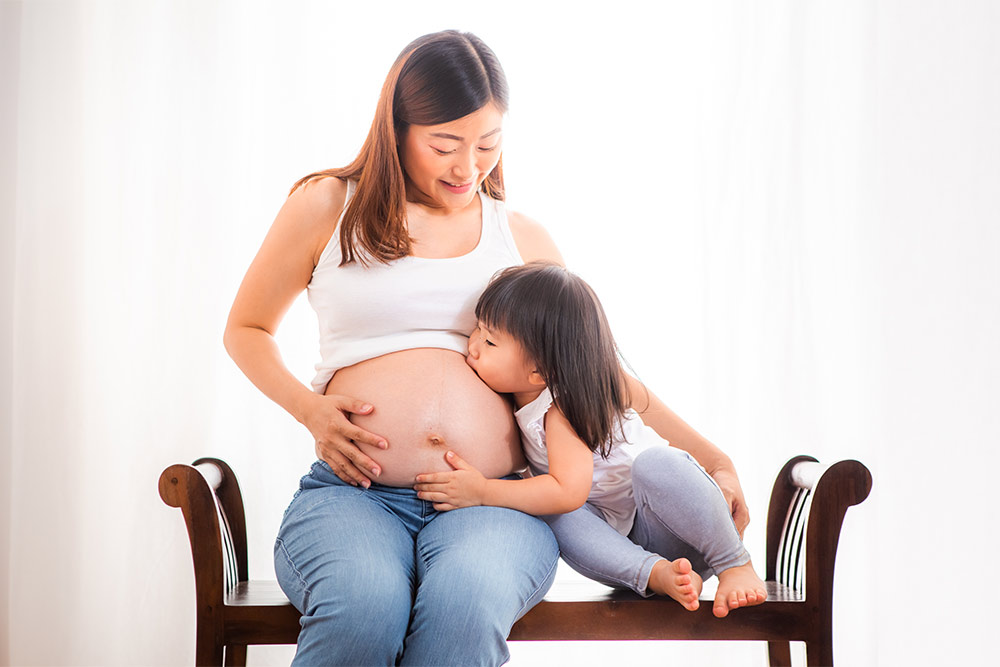 Maternity pregnant lady with toddler daughter kissing her belly