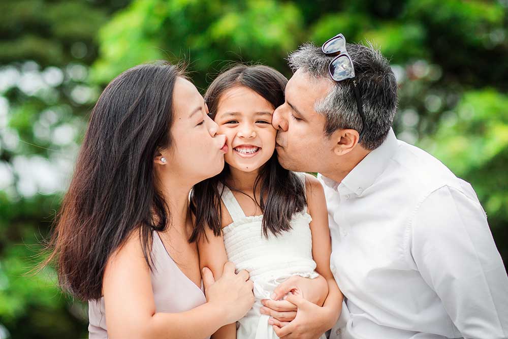 family of three kissing at greenery