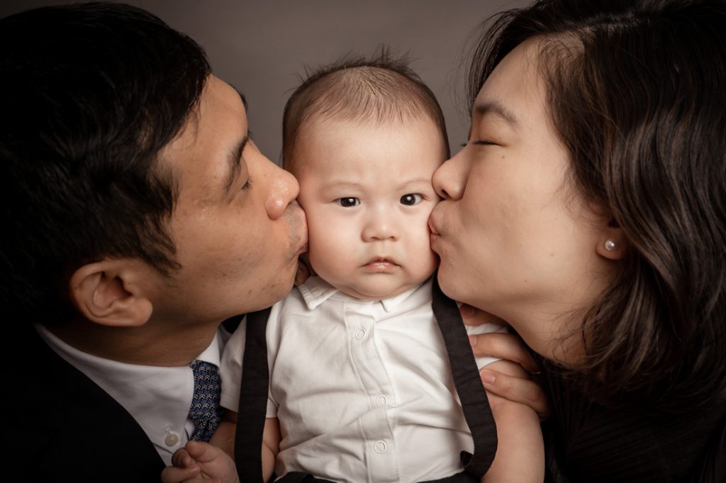 candid frowning 100 day old baby parents kissing