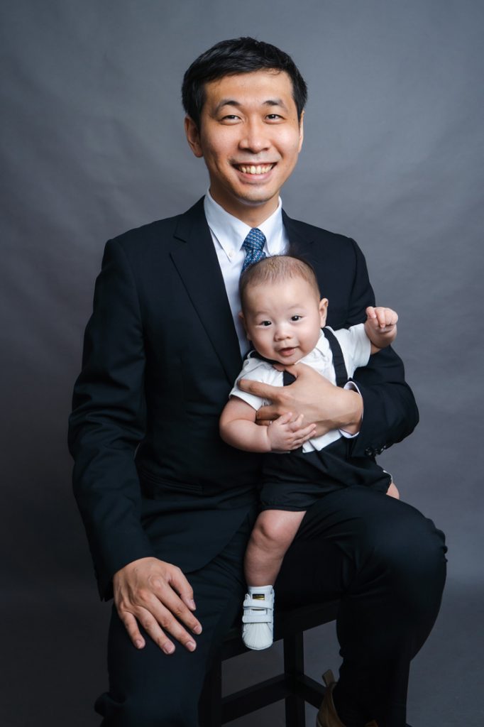 father formal smiling with 100 day old baby photostudio