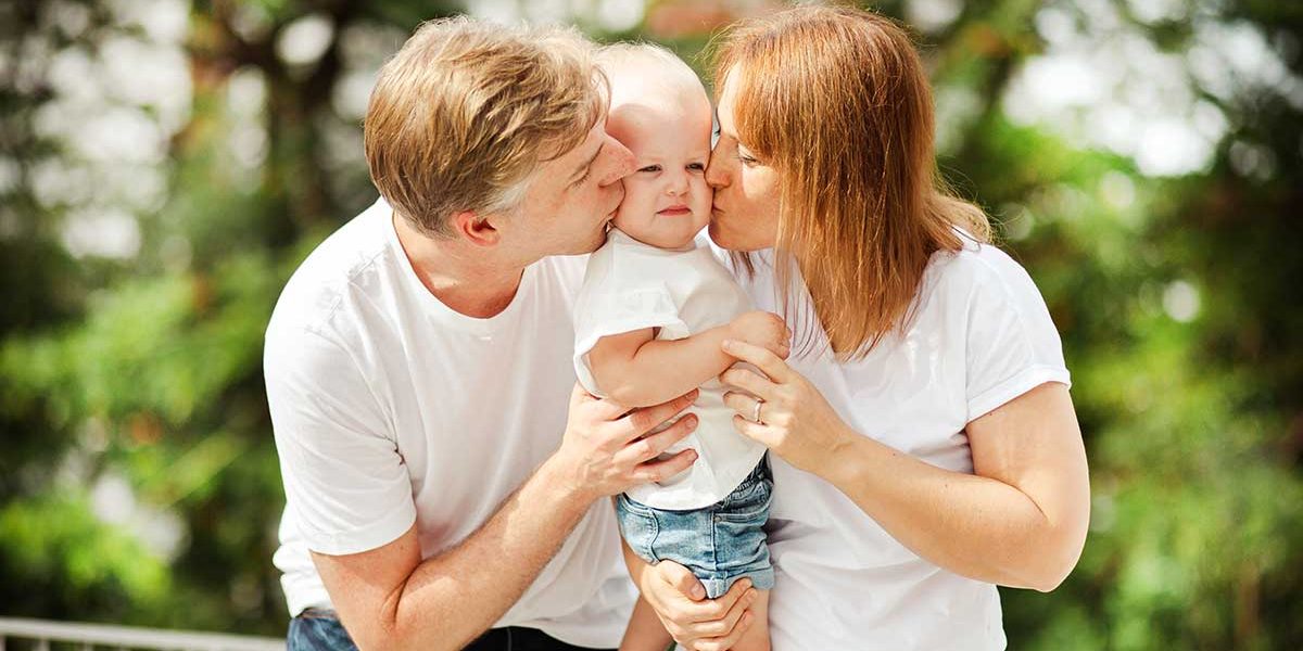 toddler-photoshoot-tips-parents-kissing-studio Toddler with parents kissing her cheeks during photoshoot