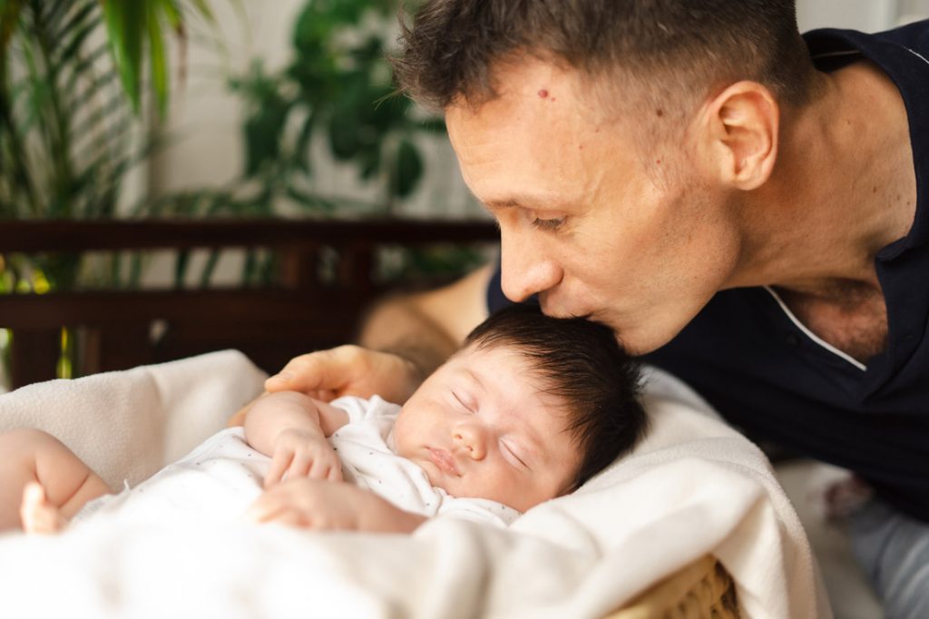 father kissing newborn infant sleeping