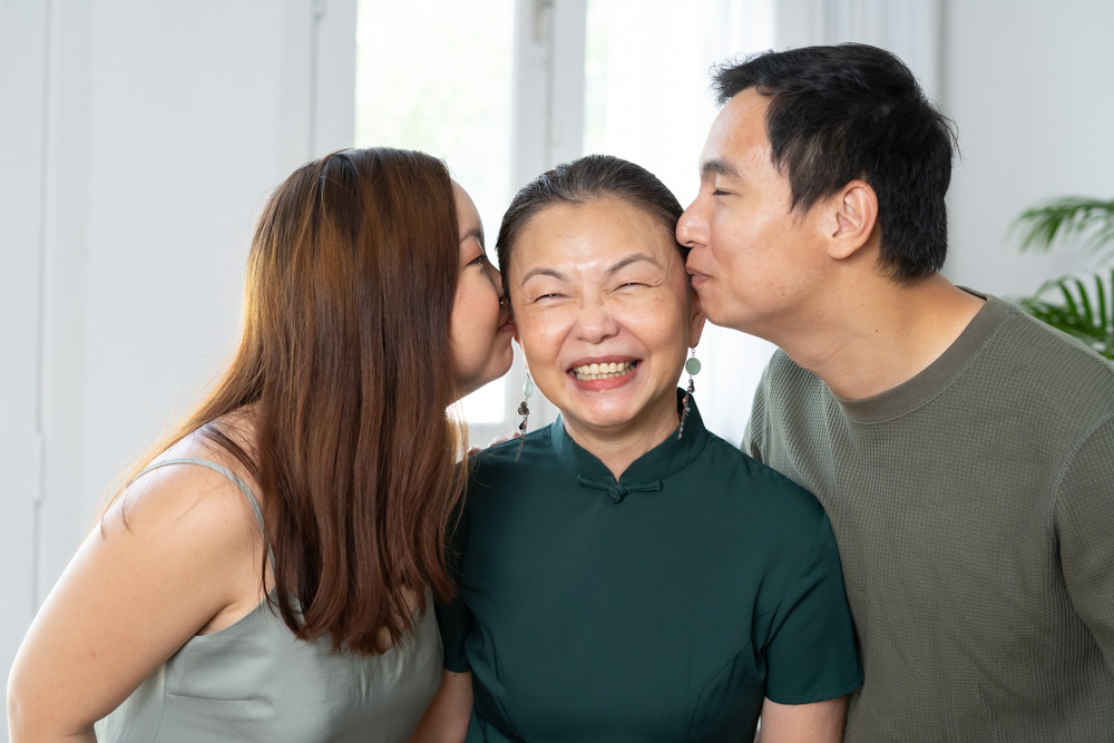 two adult children kissing elderly laughing mother