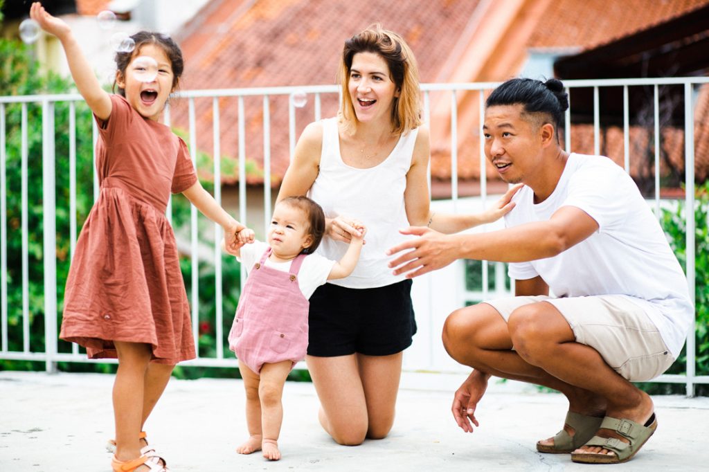 elder sister holding baby sister hands parents laughing