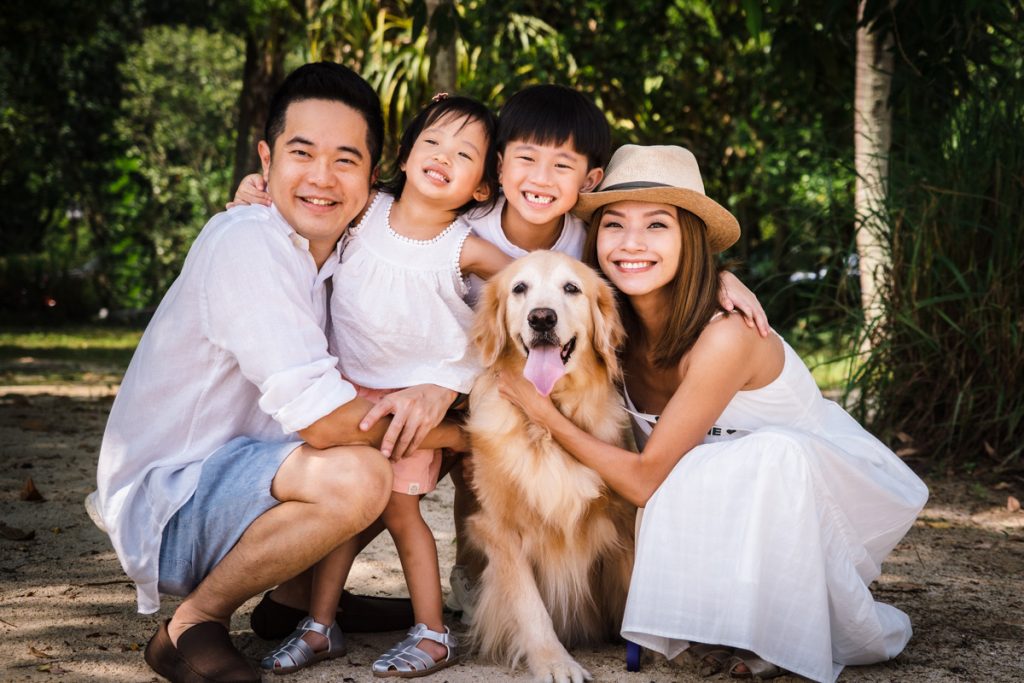 family smiling at camera outdoor photoshoot with their pet dog
