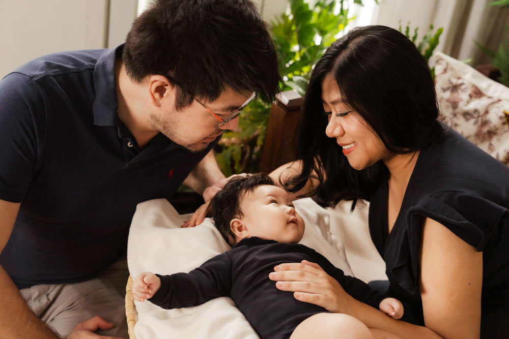 parents smiling at 100 day old baby in a basket