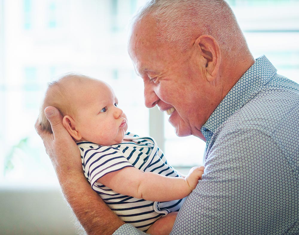 Grandfather holding and smiling at newborn baby