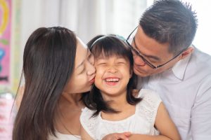 laughing 6 year old girl with parents kissing candid photoshoot